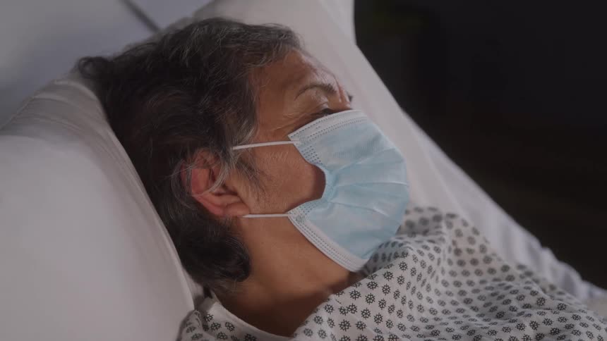 A patient lies on a hospital bed wearing a nose mask