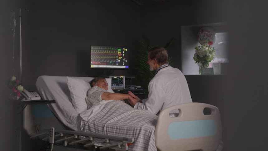 Doctor comforts a patient in a hospital bed in a dim room