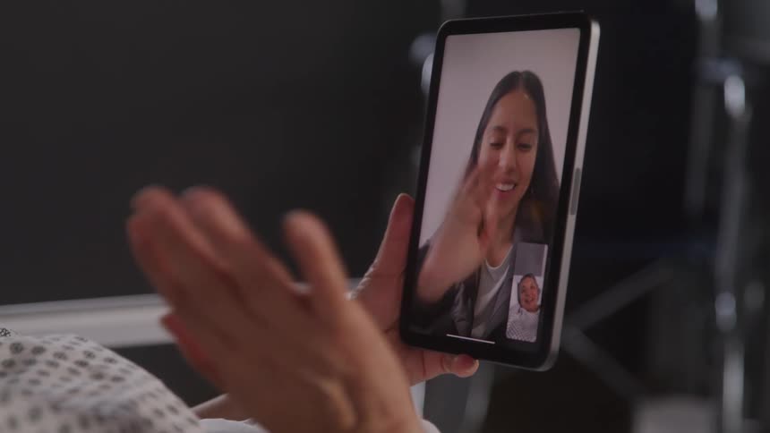 A female on a video smiles at a person holding a tablet waving at her