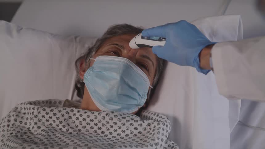 Healthcare worker checks patient temperature in hospital bed