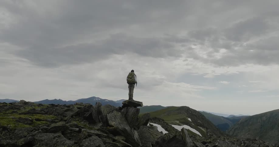 A lone hiker stands on a rock looking out over a valley
