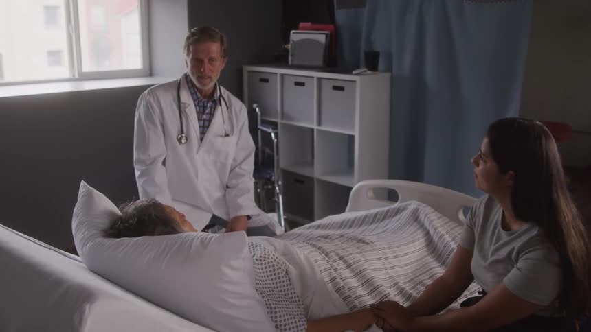 Doctor sits next to a hospital bed to talk to a patient and their family member