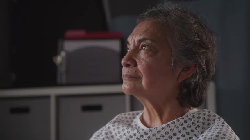 Elderly woman sits thoughtfully in a hospital room