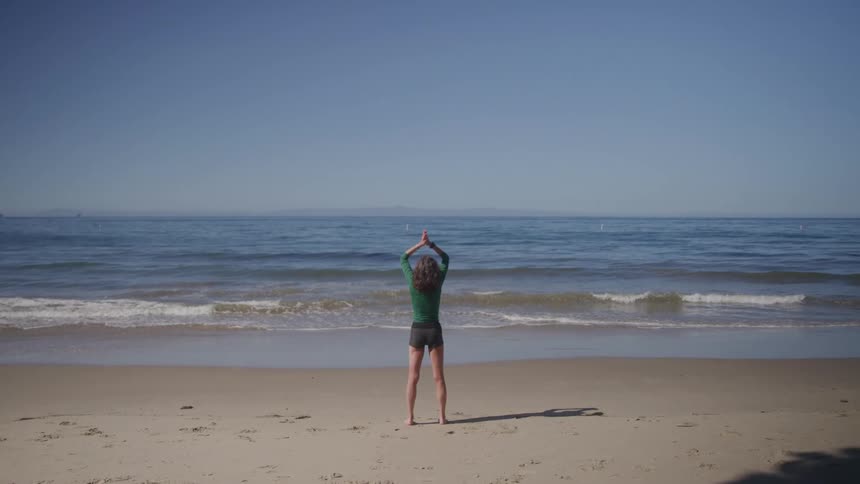 Woman standing on the sand looks out at the sea on a clear day
