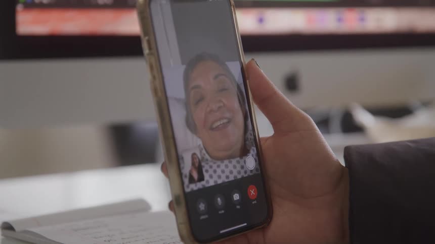 A person holds a phone during a video call with an elderly woman who appears excited and happy