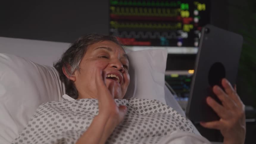 A female patient lies on a hospital bed having a video call on an ipad