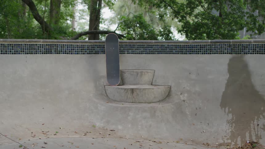 Skateboard rests upright against empty pool wall