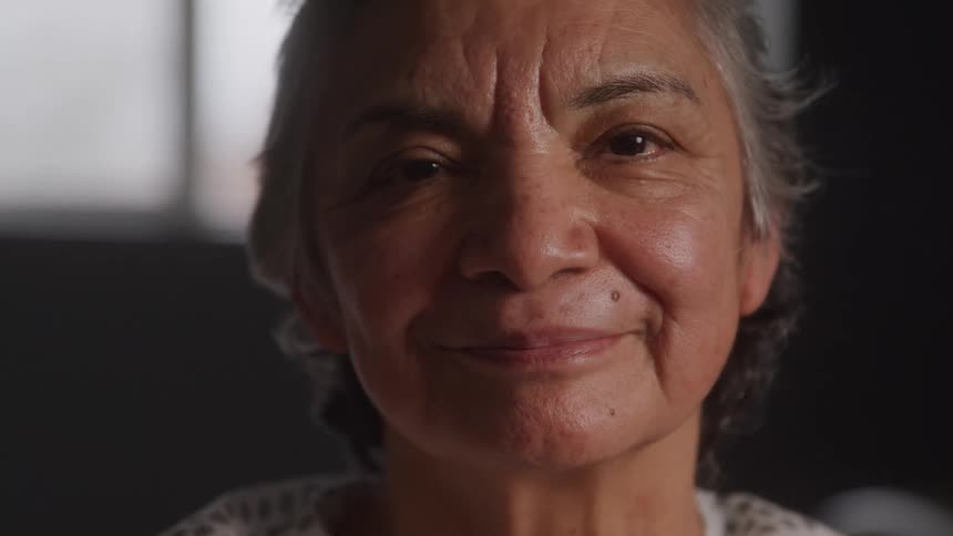 An elderly female patient sits in a hospital with a smile on her face