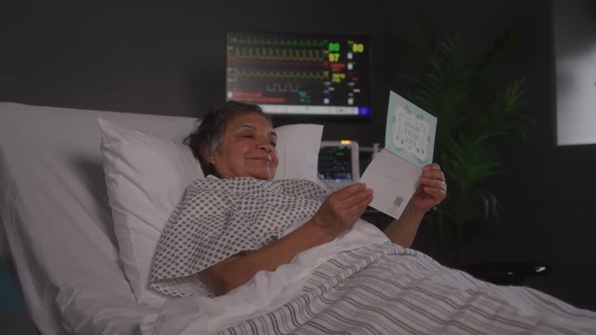 Elderly woman laying in a hospital bed reading a get well card