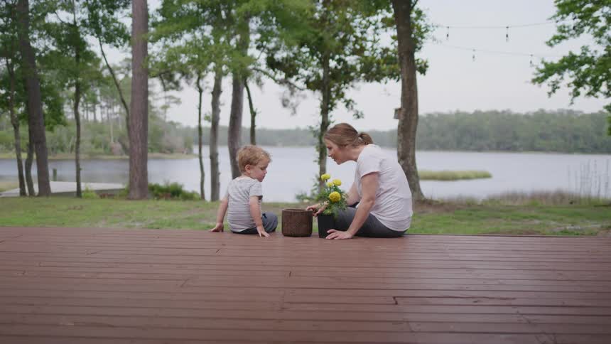 Woman and child sit on a wooden deck near a lake with trees in the background