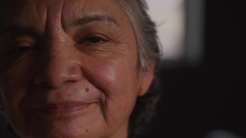 The video shows a closeup of a smiling older woman with graying hair she is looking directly at the camera with a kind and gentle expression on her face