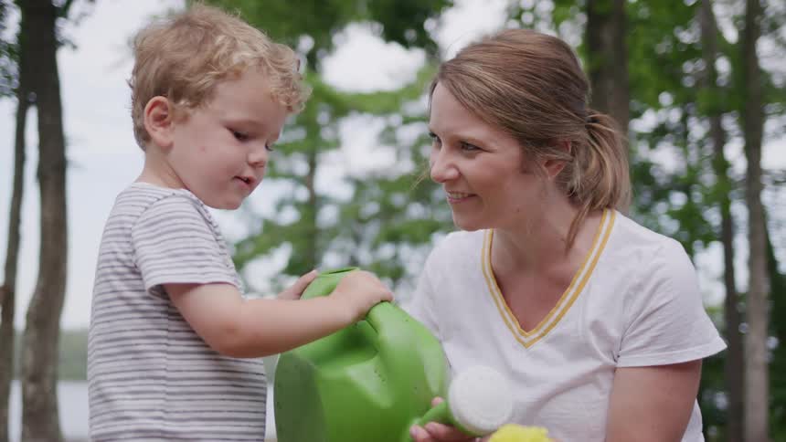 Woman smiles while helping a child hold a green watering can