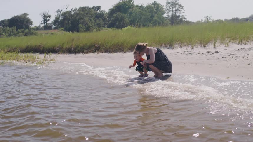A mother and son crouch as the waves hit their feet