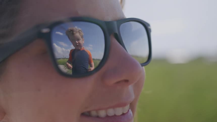 Boy in an orange shirt reflected in the sunglasses of a smiling woman