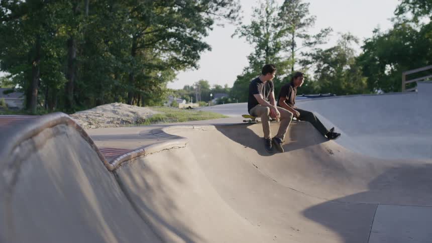 Two men sitting on the edge of an outdoor skate park