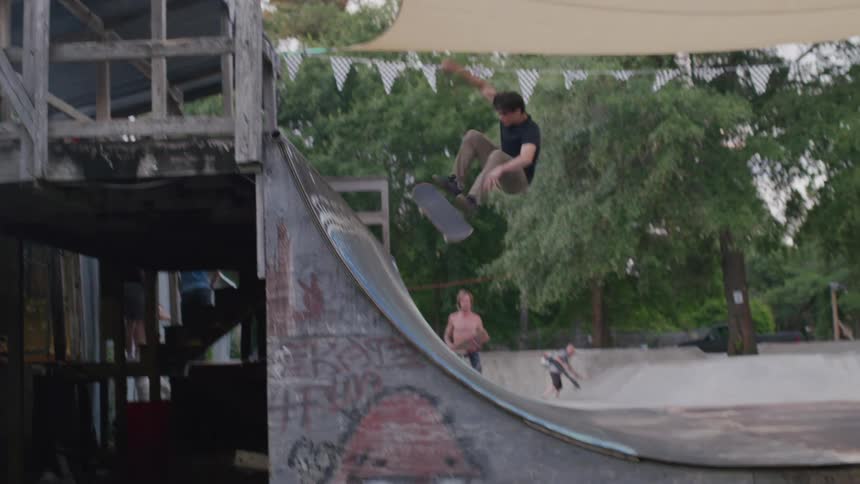A man wearing a black shirt and green pants rides a skateboard up a curved ramp at a skate park