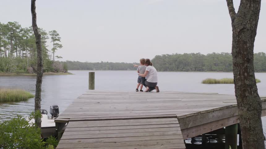Adult hugs a child on a wooden dock facing a lake