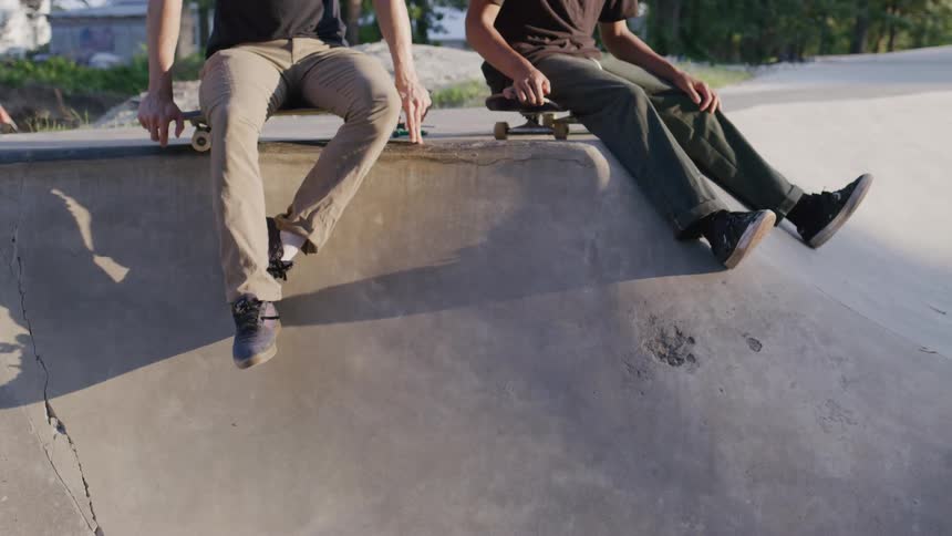 Two men sitting on the edge of a skatepark hold their skateboards