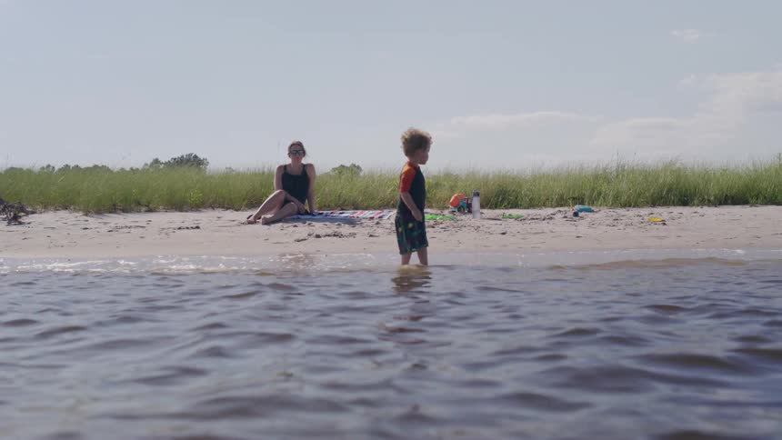 A mother watches her son play in the water