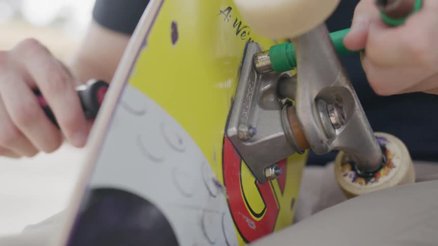 Person uses tools to tighten the bolts attaching the wheels onto a skateboard