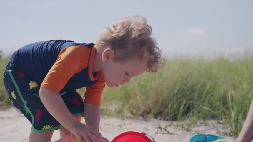 Mother digs in the sand while playing with her son and his toys on the beach