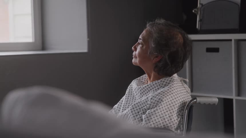 Elderly patient sitting in a wheelchair in a hospital room looking out the window