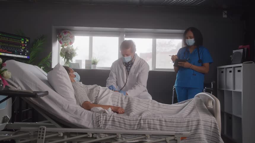 A doctor and nurse attend to a patient resting in a hospital bed