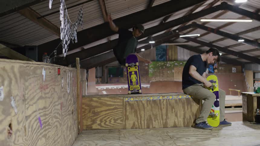 A teenager is repairing his skateboard as others ride on the ramps