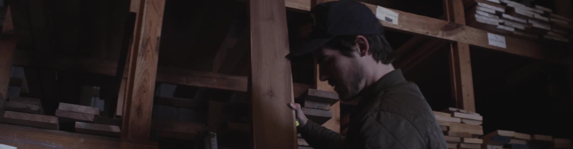 A man pulls a board from a high shelf in a dark warehouse