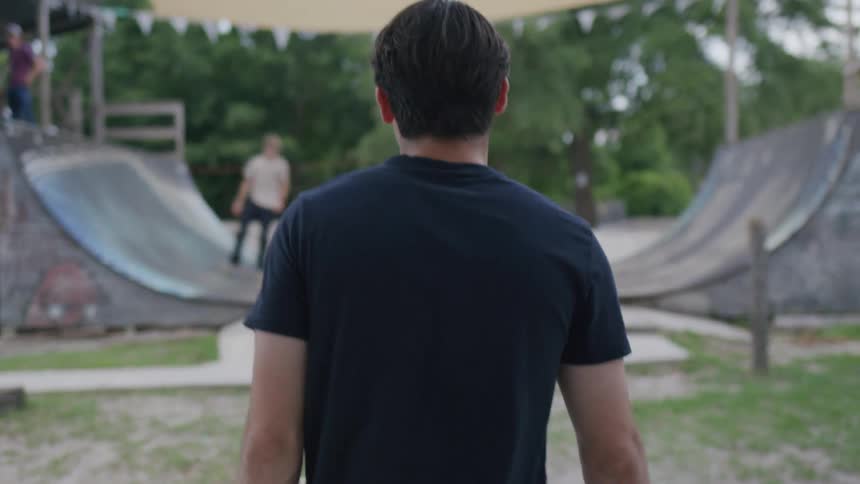 Man in a black tshirt walks toward an outdoor skate ramp