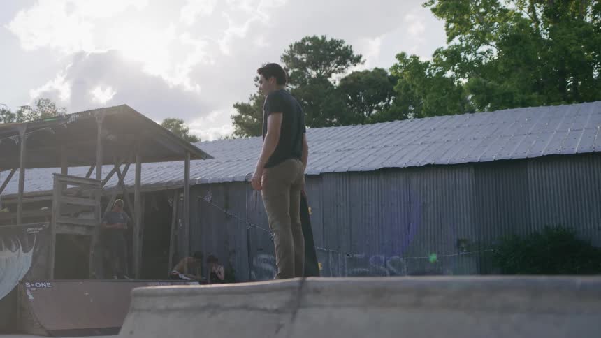 Man stands watching the outdoor skate park near a shed
