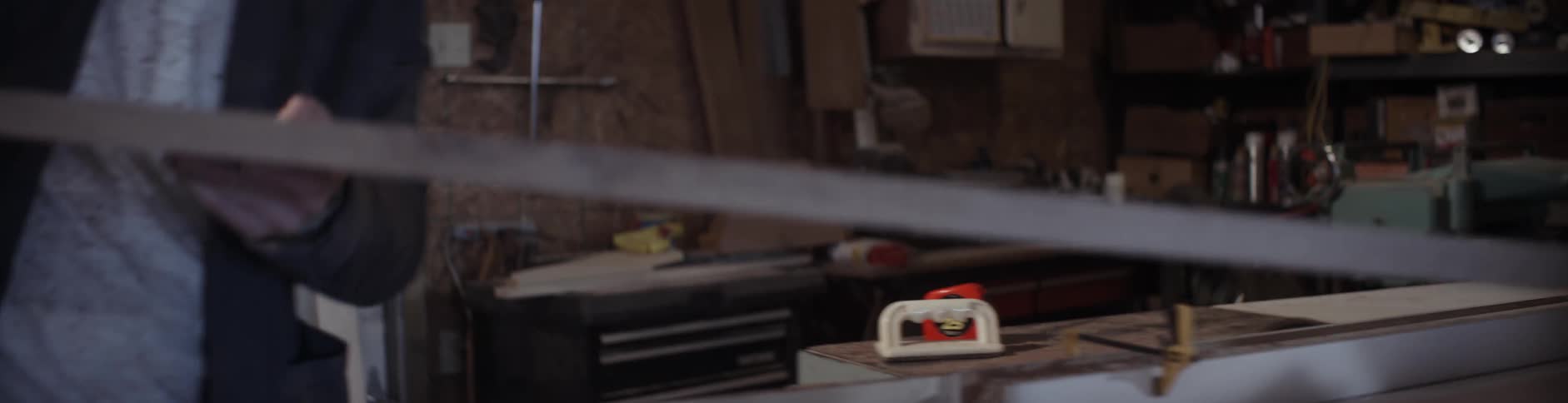 A man carries a board over to a workbench