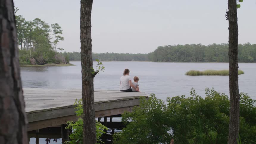 A mother and son are sitting on the pier watching the water