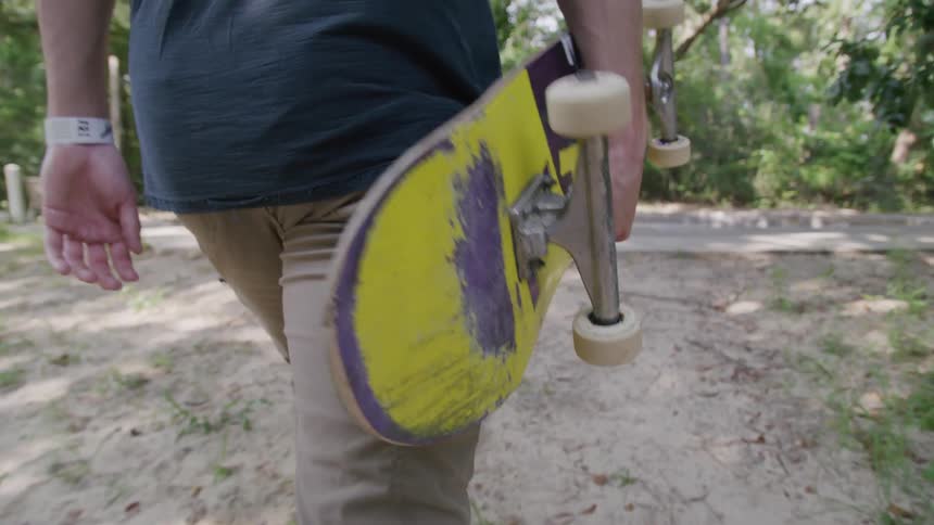 The man carries his skateboard over to the empty pool