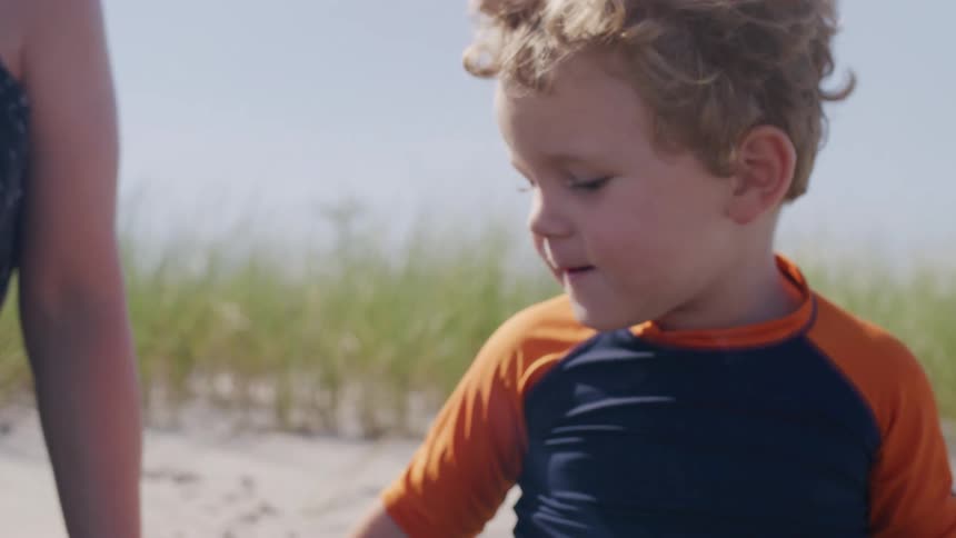 Boy in a blue and orange shortsleeve shirt plays in the sand at the beach