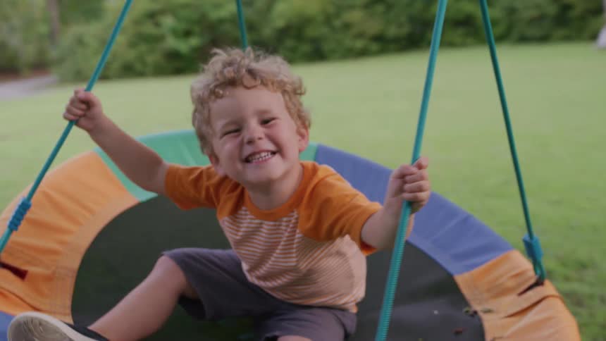 A young boy happily swings on a circular outdoor swing in a park