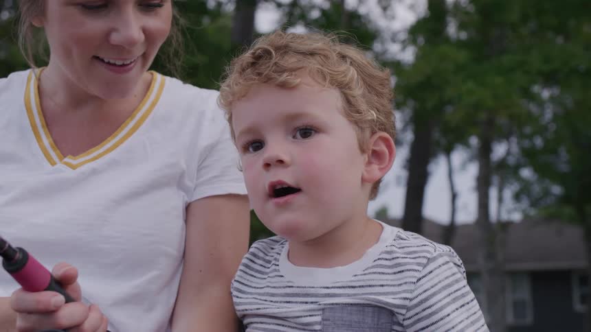 Mother next to her young son watches attentively outdoors