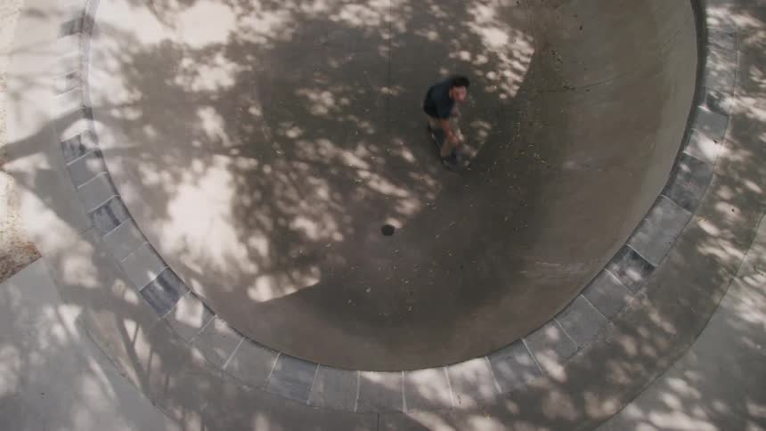 A young man skateboards on a vert ramp in a skateboard park at midday