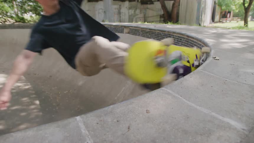 A male skateboarder swiftly grinds along the concrete coping of an empty bowlshaped pool on a sunny day