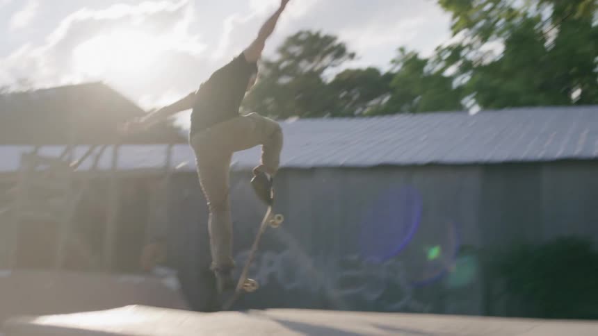 A skateboarder performs a high jump trick in the sunlit skate park with dramatic lens flare