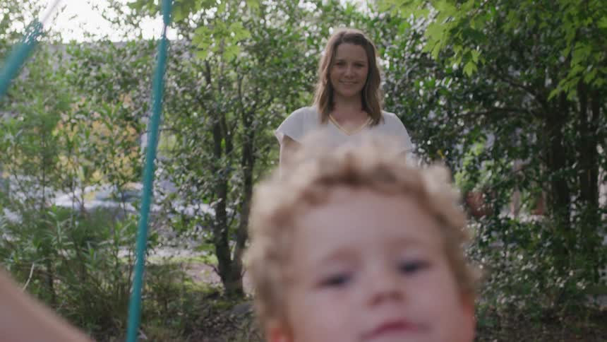 A woman smiles as she pushes a small boy with curly hair on a circular multi colored swing