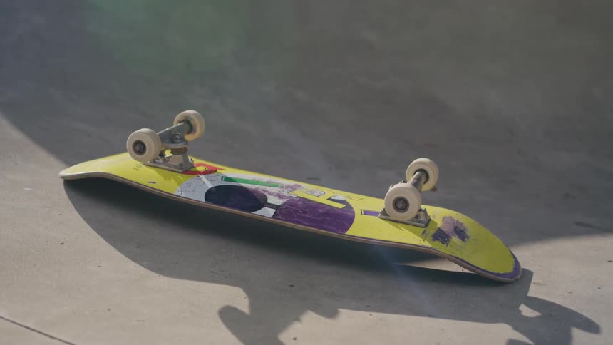 Yellow skateboard with purple details lies on its side in a concrete skatepark