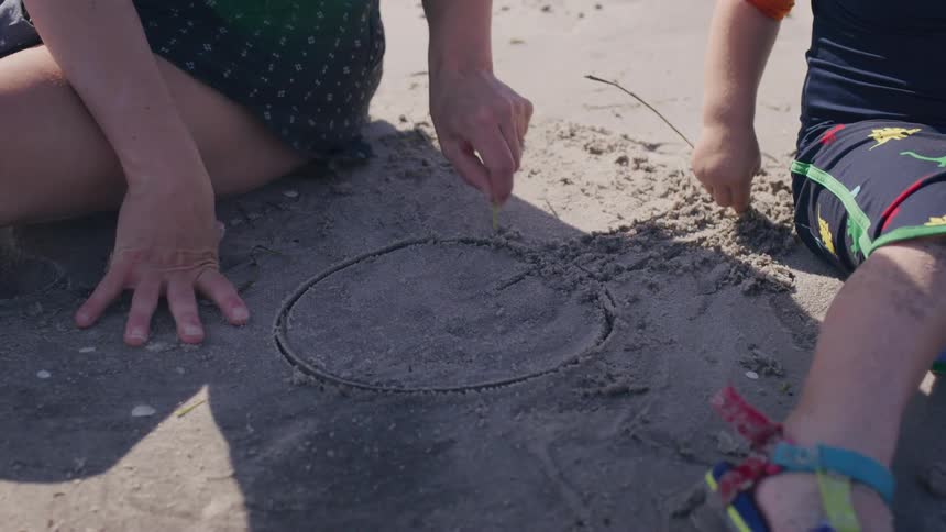 Mother and small child drawing on the sand with twigs