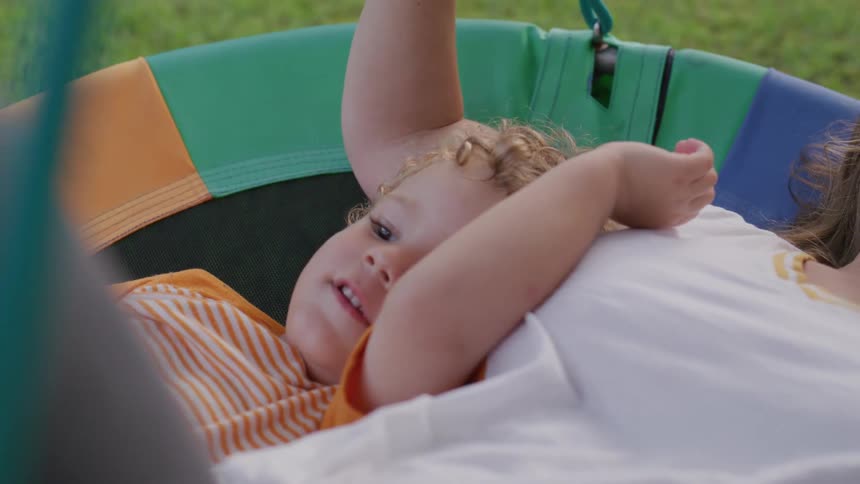 Smiling child in a colorful swing with mom outdoors