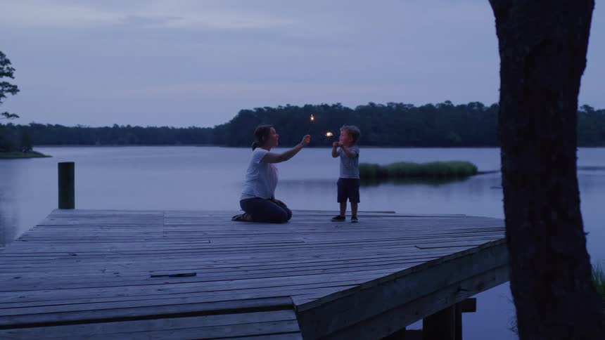 Woman and child light sparklers on a pier at dusk