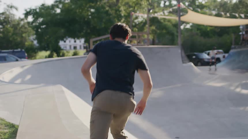 The video shows a young man with a black shirt and dark hair standing in a skatepark he is turned away from the camera looking at the concrete ramps and bowls in front of him