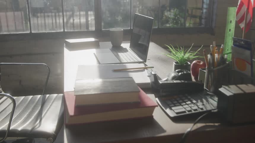 Work desk with books laptop and school supplies lit by window light