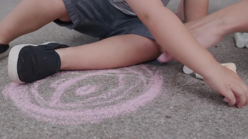 Child and adult draw a smiling face on the ground with colored chalk