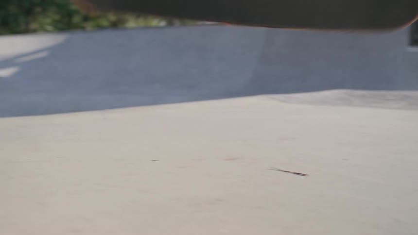 A man performs a trick on a skateboard while riding a vert ramp in a skateboarding park at midday