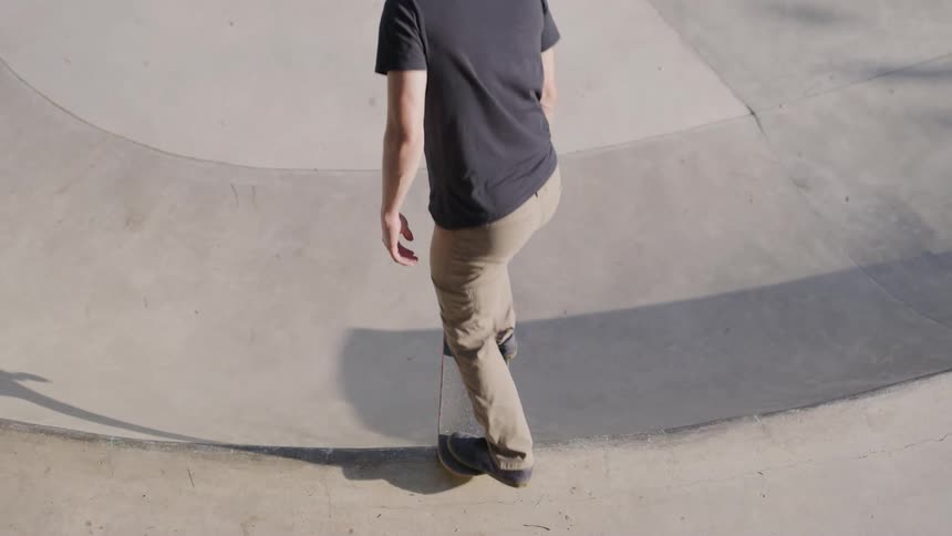 A man wearing a dark t shirt and light pants rides a skateboard into a curved concrete bowl at a skate park